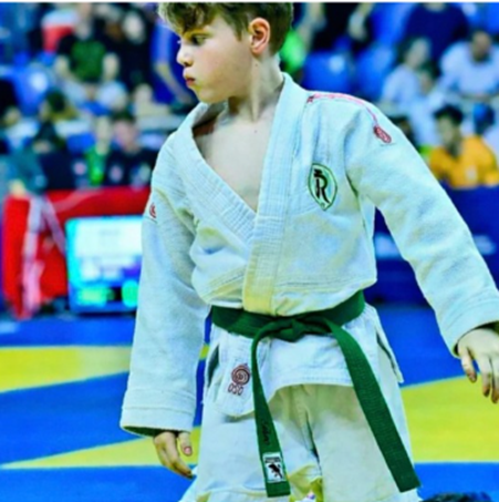 Theo Bonetto de kimono branco e faixa verde, concentrado durante competição