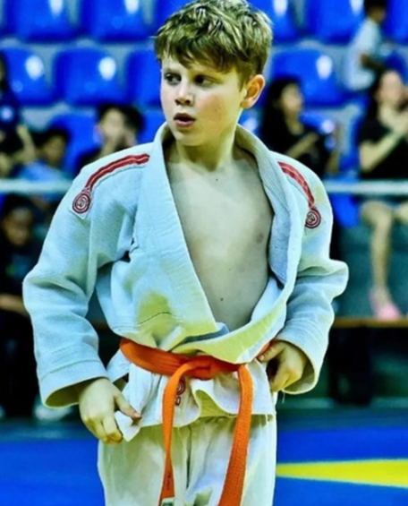 Theo Bonetto de kimono branco e faixa laranja em ginásio de competição