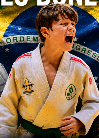 Theo Bonetto comemorando vitória de kimono branco com a bandeira do Brasil ao fundo